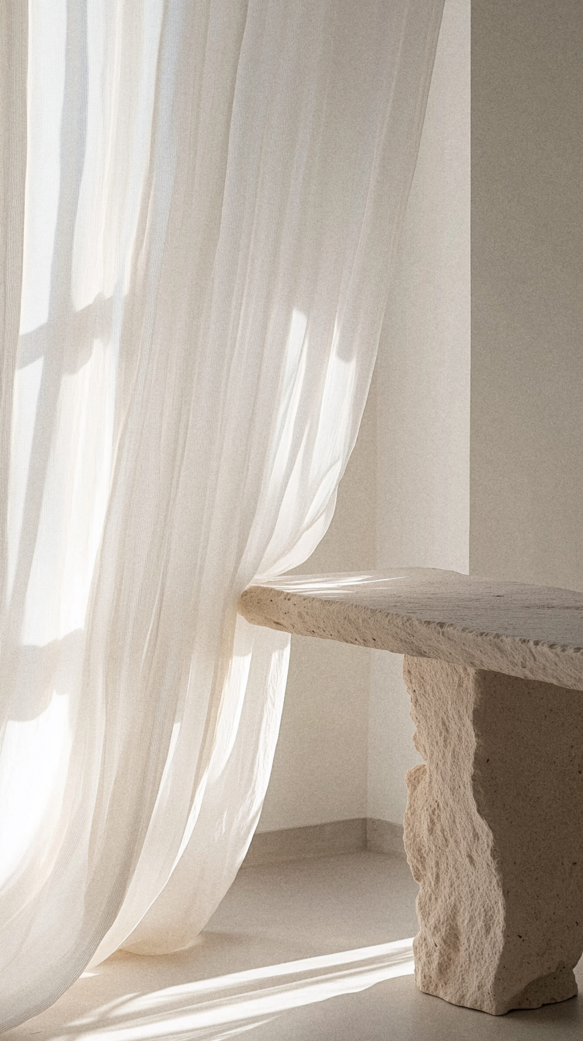 Sheer white curtains beside a stone table in soft daylight