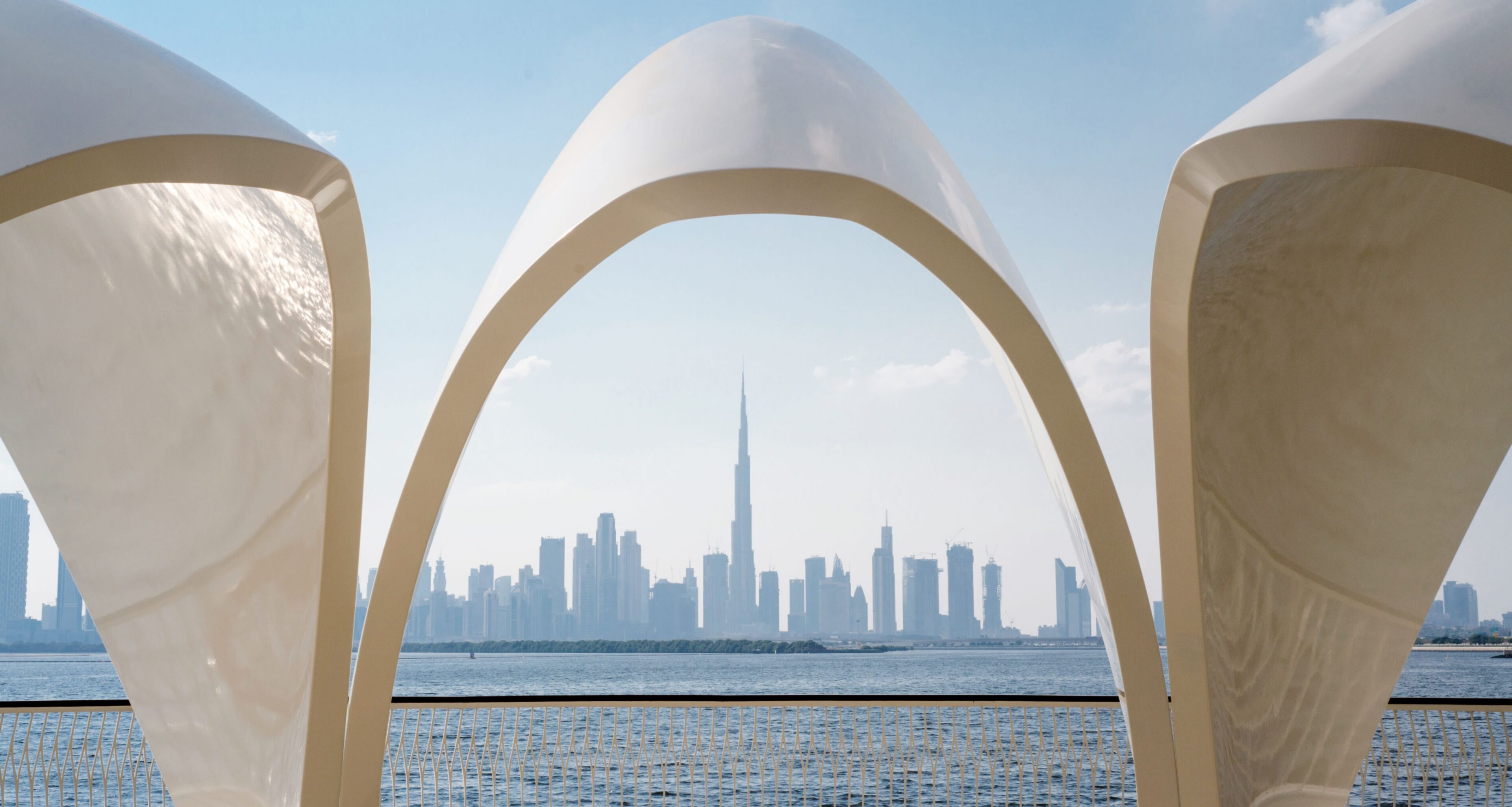 Dubai skyline with the Burj Khalifa, seen through a curved white arch across the water